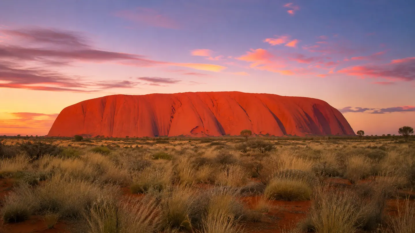 Illustration réaliste d’Uluṟu dans la lumière rouge du soir, vu depuis une distance respectueuse